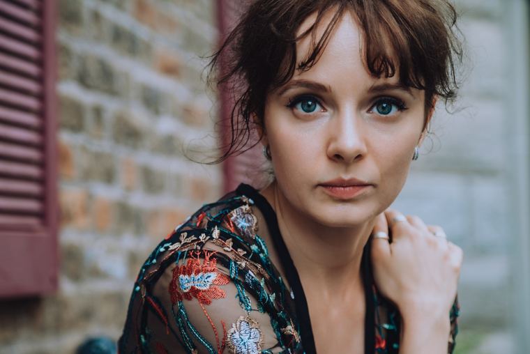 Olya in a floral lace top against a brick wall