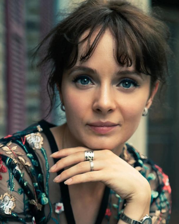 Olya in an embroidered floral top, chin on her hand